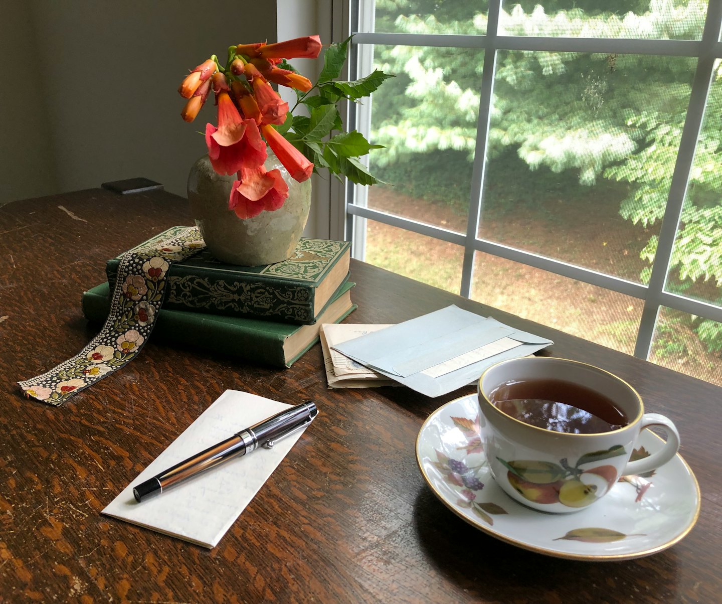 Scrivania con libri, fiori e una penna stilografica.